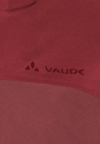 Tuvumā ir sarkana auduma daļa ar melnu Vaude zīmolu un kalnu formas simbolu uz tekstūras āra aprīkojuma.