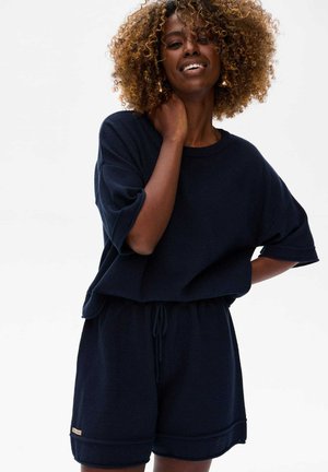 Navy blauwe gebreide lounge set met een relaxte korte mouw top en shorts met trekkoord. Gelaagde stof met contrasterende zomen.