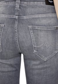 Jeans de mezclilla gris con una textura suave, que cuentan con un diseño clásico de cinco bolsillos, detalles de costura y un parche de logo en la cintura trasera.