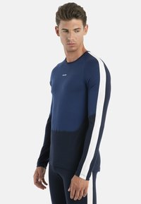 Navy long-sleeve shirt with white side stripes, made of soft fabric. Seamless design with rounded neckline and contrasting panel at waist.