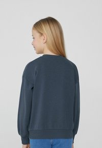 Tmavě námořnická mikina s kulatým výstřihem a žebrovanými manžetami. Má uvolněný střih, jemnou strukturu a minimalistický design.