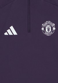 Purple athletic top featuring a half-zip design, with a white Adidas logo and Manchester United crest prominently displayed. Soft texture.