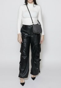 Pantaloni cargo in ecopelle nera con vestibilità ampia, dotati di tasche laterali e chiusure a scatto. Abbinati a un dolcevita bianco e a una borsa grigia.