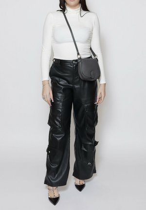 Zwarte neplederen cargobroek met een losse pasvorm, voorzien van zijzakken en drukknoopsluitingen. Gecombineerd met een witte coltrui en een grijze handtas.