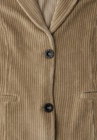 Blazer en velours côtelé marron avec texture côtelée verticale, revers crantés et deux poches avant. Comprend un bouton noir avec l'inscription "STREET".