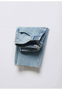 Jean en denim bleu clair plié sur une surface blanche avec des ourlets effilochés et des détails visibles des poches avant et de la ceinture.
