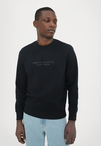 Zwart sweatshirt met een ronde hals, lange mouwen en een bedrukt logo met de tekst "ARMANI EXCHANGE MILANO / NEW YORK" in het midden.
