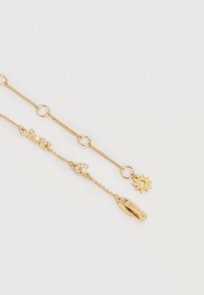 Βραχιόλι από χρυσή αλυσίδα με κυκλικά κρίκους, μικρές πέρλες και κρυσταλλικές διακοσμήσεις, με γοητευτικό μενταγιόν σε σχήμα ήλιου και κούμπωμα με λογότυπο, σε λευκό φόντο.