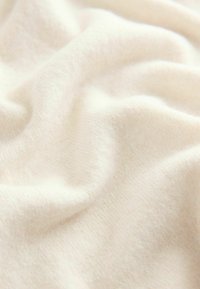 Tissu doux de couleur crème avec une texture lisse, présentant des fibres fines et subtiles ainsi que des plis délicats créant un drapé fluide.