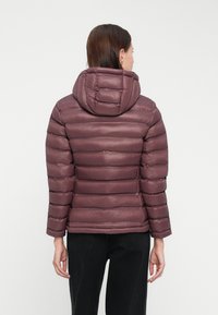 Bundička s kapucňou v tlmených fialových odtieňoch, s horizontálne prešitou štruktúrou. Materiál má hladký, jemne lesklý povrch.