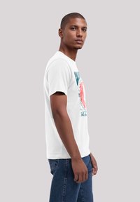 White cotton t-shirt featuring a colorful graphic print on the front, short sleeves, and a classic crew neckline, worn with blue jeans.