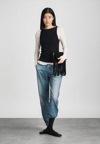 Haut sans manches côtelé noir superposé sur une chemise à manches longues beige, associé à un jean bleu clair décontracté et à un sac à franges noir. Chaussures plates noires.