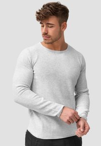 Lichtgrijze longsleeve shirt met een ronde hals, textuurstof, aansluitende mouwen en een gebogen zoom, gedragen met donkere broek.