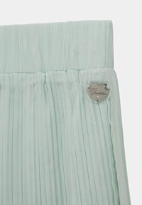 Tessuto plissettato verde menta con finitura testurizzata; presenta un badge in argento a forma di cuore con inciso "Guess".