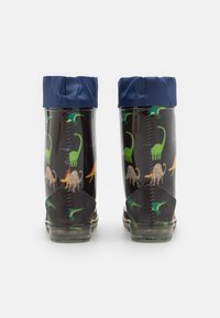 Les bottes de pluie noires présentent une semelle texturée, un rebord imperméable bleu et un motif de dinosaures coloré en vert, orange et beige sur les côtés.