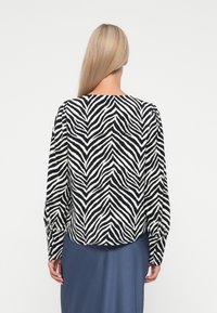 Blouse à imprimé zèbre noir et blanc avec manches longues, col rond et détails froncés aux épaules. Texture de tissu lisse.