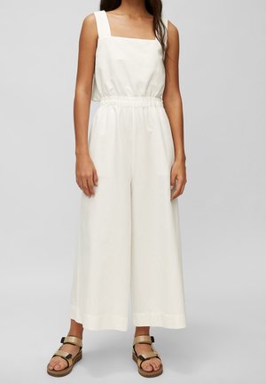Witte, mouwloze jumpsuit met een vierkante halslijn, elastische tailleband, brede benen en een gladde stofstructuur. G gedragen met bruine sandalen.