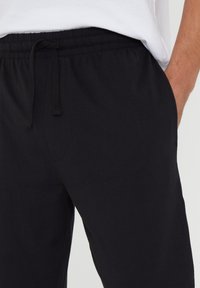 Sorte sweatpants med elastisk talje og justerbar snøre. Har sidelommer og en glat, tekstureret stof.
