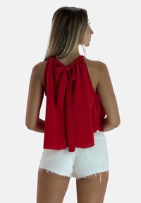 Rode mouwloze top met een geplooide hals en strikdetail aan de achterkant, gecombineerd met witte shorts met rafels aan de onderkant. Gladde stofstructuur.