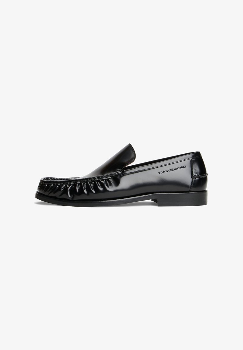 Mocassin noir en cuir brillant avec design moc toe cousu et petit talon, avec le logo Tommy Hilfiger sur le côté.