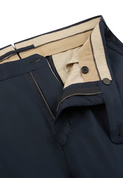 Pantaloni blu navy con fodera interna beige, volata con zip aperta e chiusura con bottone visibile in vita.