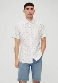Kurzarm-Hemd aus weißer Baumwolle mit kleinem Blumenmuster, ausgestattet mit einer Brusttasche und einem umklappbaren Kragen, kombiniert mit Jeansshorts.