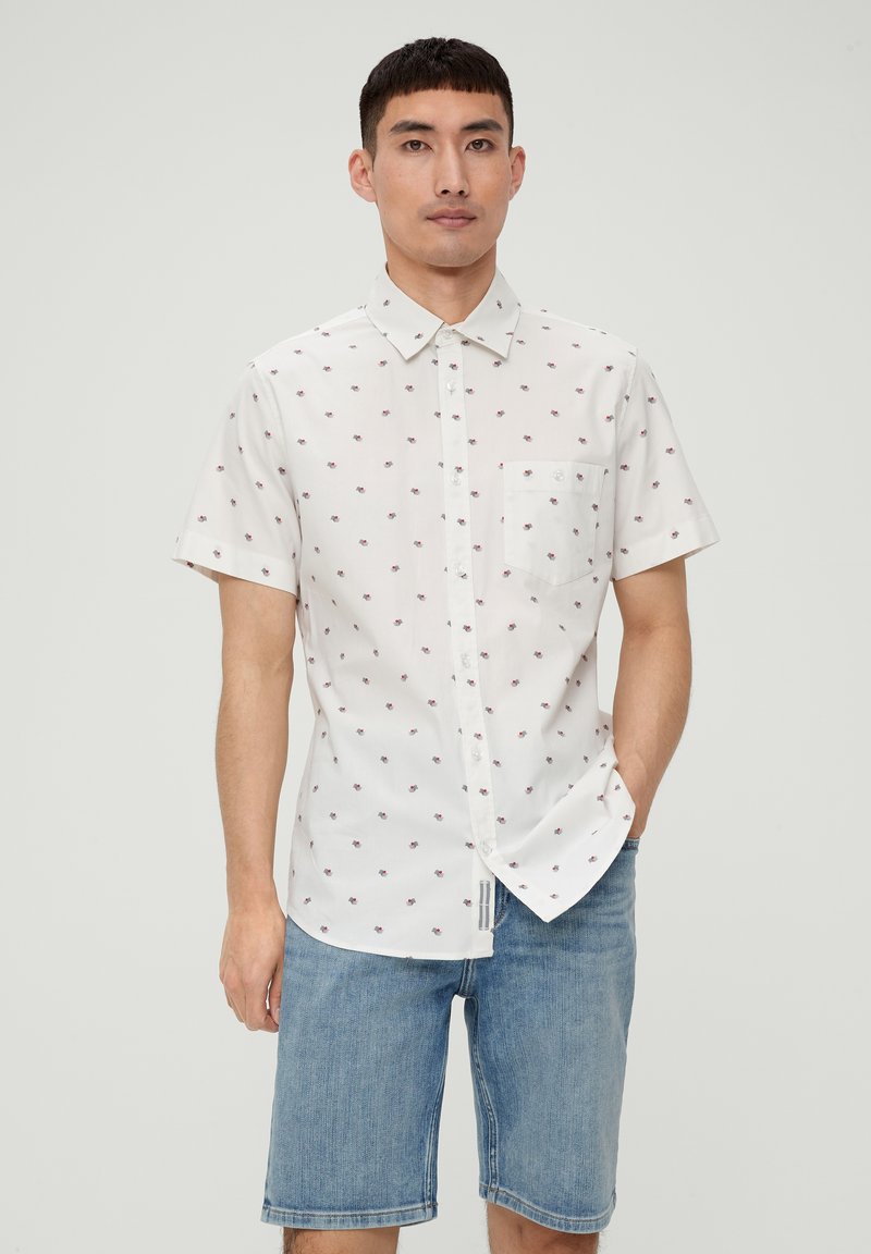 Kurzarm-Hemd aus weißer Baumwolle mit kleinem Blumenmuster, ausgestattet mit einer Brusttasche und einem umklappbaren Kragen, kombiniert mit Jeansshorts.