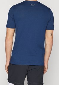 Mörkblå T-shirt med kort ärm och rund halsringning samt mjuk textur. Har en logotyp på baksidan, kombinerad med svarta träningsshorts.