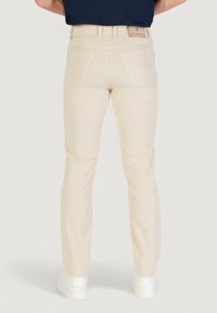 Jeans beige con vestibilità slim, due tasche posteriori, una texture sottile e un'etichetta sulla vita, abbinati a sneakers bianche.