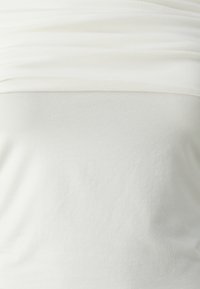 Primo piano di un top bianco senza spalline in tessuto a coste, con il bordo superiore ripiegato, su una superficie liscia.