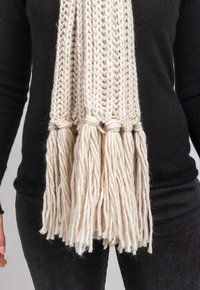Cremefarvet strikscarf med en chunky tekstur, der har lange frynser i bunden og et enkelt, ribbet design.