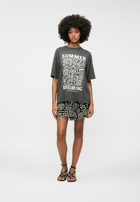 T-shirt gris oversize avec l'inscription blanche "SUMMER DREAMING", associé à une mini-jupe noire à motifs et des sandales noires à lanières.