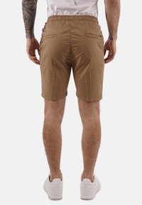 Pantaloni corti color khaki realizzati in tessuto leggero, con vita elasticizzata, tasche laterali e orlo piatto. Indossati con sneakers bianche.