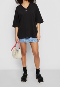 T-shirt nera oversize con scollo a V, minigonna in denim, borsa beige con fasce rosa e scarpe nere con strap in velcro e suola rosa.