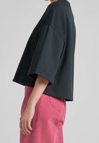 Sudadera negra corta con mangas anchas, con un detalle de logo texturizado en la parte frontal. Combinada con pantalones de pierna ancha en rosa claro.