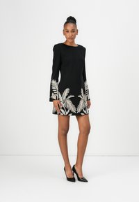 Black dress with long sleeves and a round neck. Features white palm leaf embroidery at the hem. Smooth fabric, fitted silhouette, knee-length.
