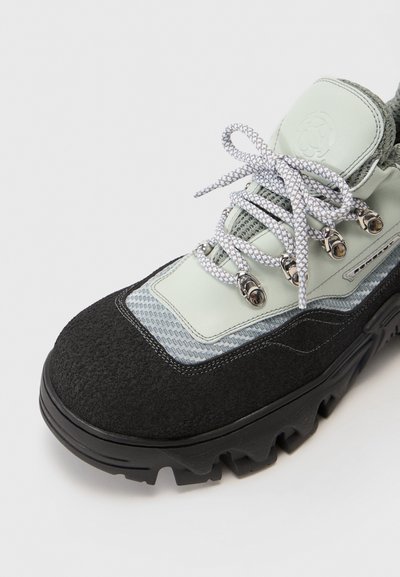 Wanderstiefel aus grünem und schwarzem Wildleder, mit einem strukturierten Netzpaneel, silbernen Beschlägen und reflektierenden Schnürsenkeln. Dicke schwarze Gummisohle.