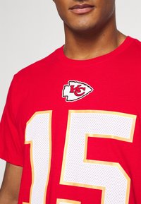 Czerwona bawełniana koszulka z okrągłym dekoltem, z białym i złotym perforowanym numerem "15" oraz logiem Kansas City Chiefs nad numerem.