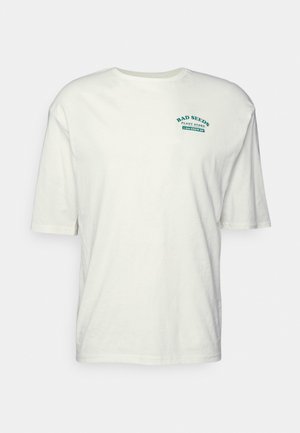 Valge puuvillane T-särk lühikeste varrukatega, ümar kaelus ja teelroheline graafikatekst "BAD SEEDS PLANT STORE" trükitud esiküljele.