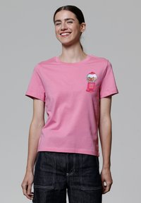 Roze katoenen t-shirt met korte mouwen. Heeft een afbeelding van een knopjesmachine op de linkerborst. Eenvoudig, recht gesneden ontwerp.