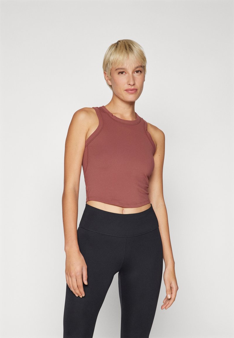 Cropped tank top in reddish-brown fabric with a round neckline and sleeveless design, paired with black high-waisted leggings. Minimal stitching detail.