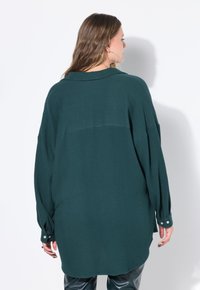 Camicia verde oversize realizzata in tessuto testurizzato, con cucitura a yoke sul retro, maniche lunghe e polsini con bottone.