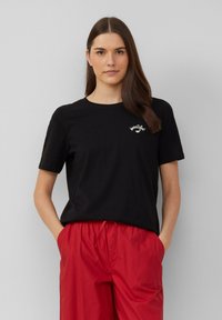 Zwarte katoenen t-shirt met korte mouwen, ronde hals en geborduurde witte tekst "beautiful". Relaxte pasvorm. Gecombineerd met rode shorts.
