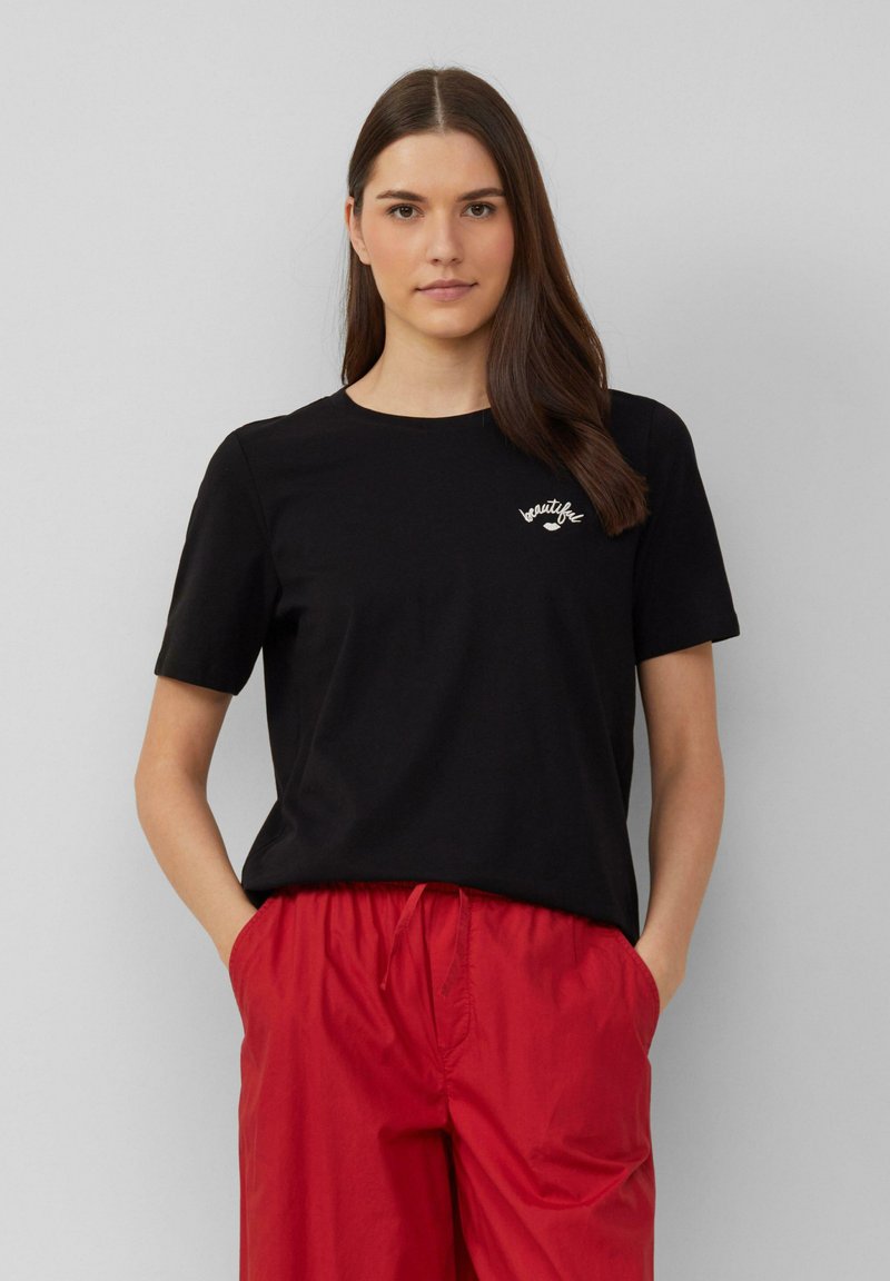 Zwarte katoenen t-shirt met korte mouwen, ronde hals en geborduurde witte tekst "beautiful". Relaxte pasvorm. Gecombineerd met rode shorts.