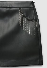 Schwarzer Lederrock mit geradem Design, ausgestattet mit einer diagonalen Tasche, die mit mehreren metallischen Ketten und Perlen verziert ist.