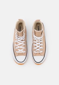 Para beżowych, wysokich trampków z płótna, z białymi sznurówkami i gumowymi podeszwami, widok z góry na białym tle.