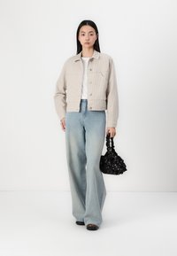 Veste en velours côtelé beige avec fermeture à boutons, associée à un jean large bleu clair et un sac noir à motif floral.