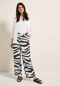 Pantalons larges en blanc avec des rayures noires de zèbre, en tissu léger, associés à un débardeur blanc et une chemise blanche transparente à boutons.