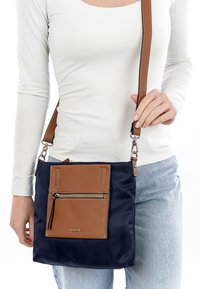 Borsa a tracolla in nylon blu navy con dettagli in pelle marrone, tasca frontale con zip, tracolla regolabile e accessori in argento. Dettagli in pelle texturizzata evidenziati.