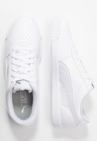 Bílé atletické boty vyrobené z syntetické kůže s texturovaným povrchem. Mají kulatou špičku, ploché tkaničky a decentní branding na stélce.